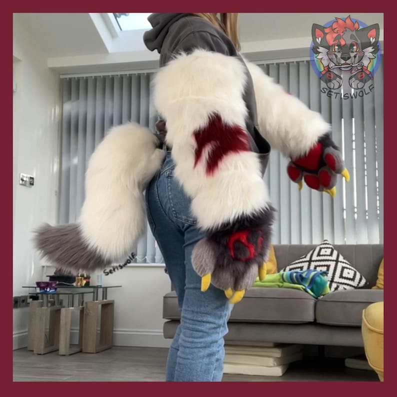 May include: Furry costume paws and tail set. The paws are white with red and gray accents, yellow claws, and a red emblem. The tail is white and gray. The set is designed to be worn as part of a costume.