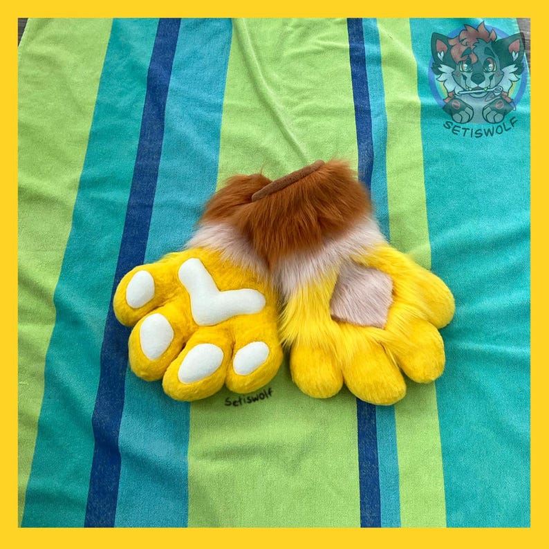 May include: A pair of plush, yellow faux fur hand paws featuring white paw pads and a brown fur cuff at the wrist. The design includes a soft, textured appearance with distinct finger sections and a rounded shape, crafted for costume use.