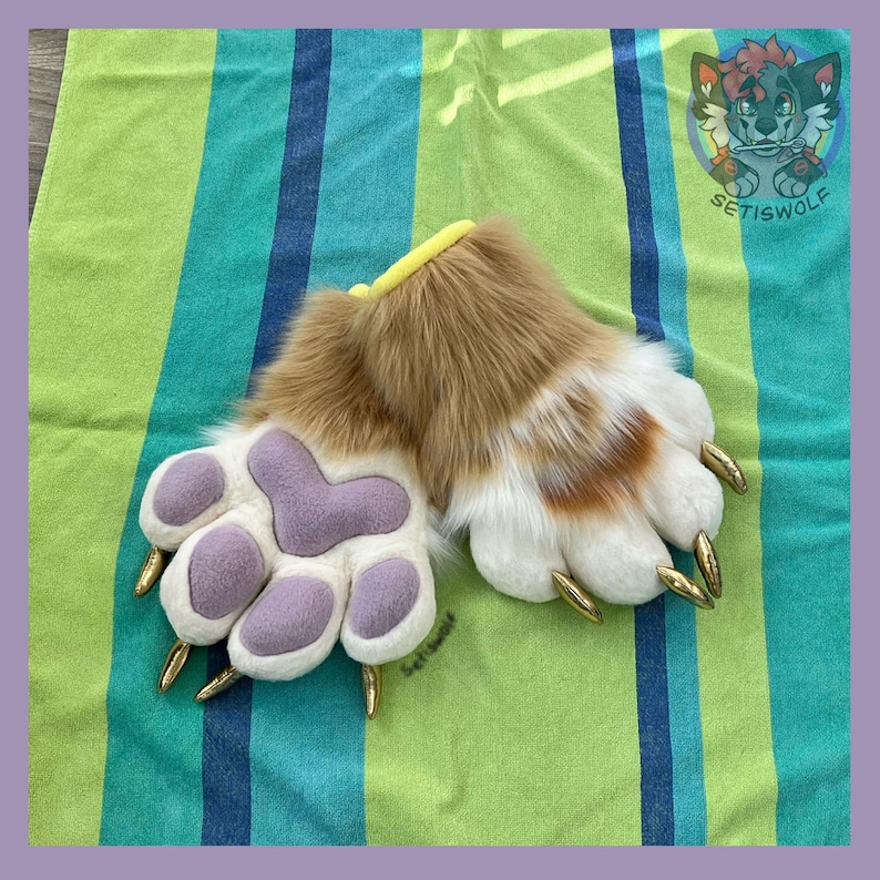 May include: A pair of plush animal paw gloves featuring long tan and white faux fur, soft lavender fabric paw pads, and pointed gold-colored claws. The wrist openings are trimmed with a yellow band, and the design includes a cartoon wolf logo.