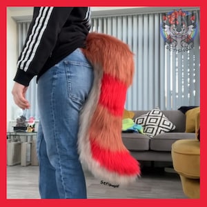 May include: A furry, red, orange, and white tail prop. The tail is attached to a person wearing blue jeans. The tail has a striped pattern and is made of faux fur. The tail is a costume accessory.