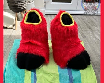 May include: A pair of plush, ankle-high footwear featuring vibrant red faux fur covering the upper section and solid black rounded toe caps. The openings are lined with a bright yellow trim, and the interior is lined with black fabric.