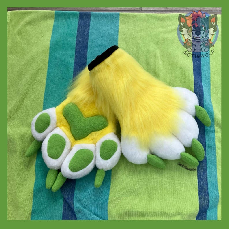 May include: A pair of plush hand paws featuring bright yellow faux fur, white paw pads, and green accents on the palm and fingertips. The wrist openings are trimmed with black fabric. A small logo with a wolf illustration is visible in the corner.
