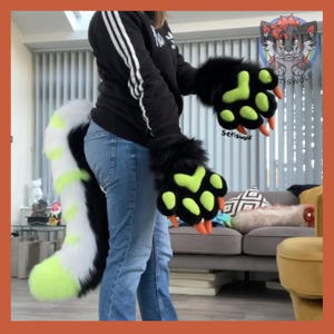 May include: Black and green furry paw gloves with orange claws and a matching tail. The tail is white with black and neon green stripes. The gloves and tail are part of a costume. The text "Setiswolf" is visible on the gloves.