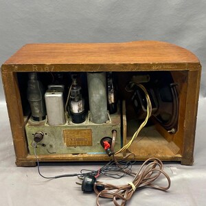 May include: A vintage wooden radio with a brown finish. The radio has a metal front panel with a speaker and several knobs. The radio is open and shows the internal components, including tubes and wires.