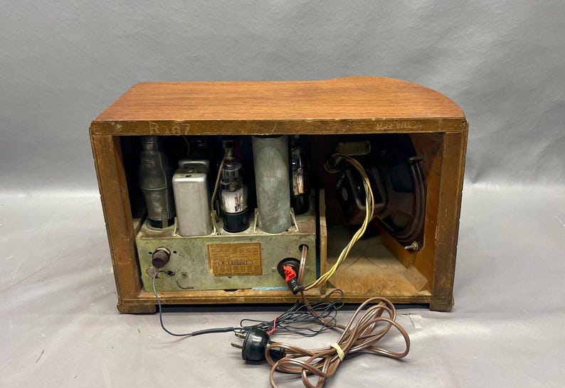 May include: A vintage wooden radio with a brown finish. The radio has a metal front panel with a speaker and several knobs. The radio is open and shows the internal components, including tubes and wires.