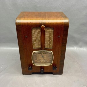 May include: A vintage wooden Emerson radio with a gold-colored dial and a woven speaker grille. The radio has a brown wooden cabinet with a black knob on each side.