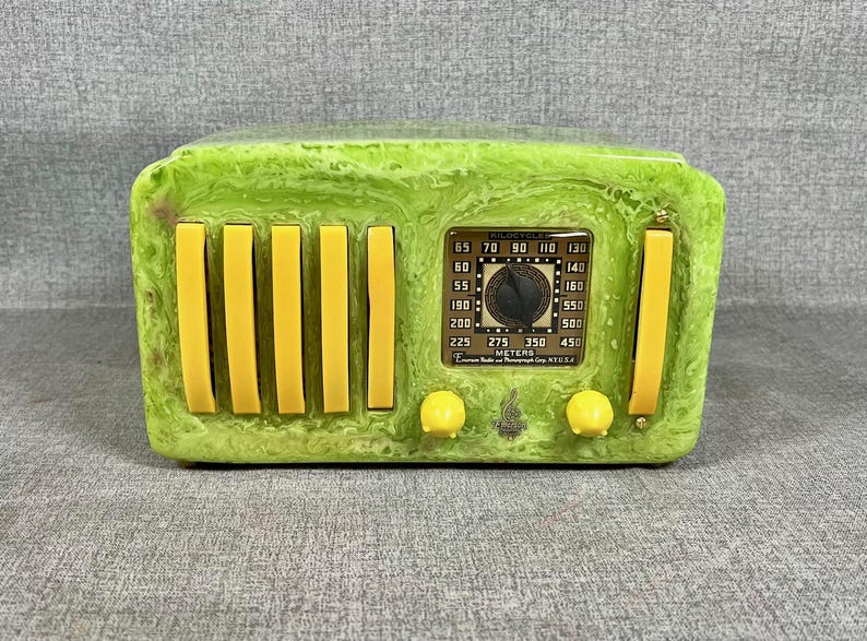 May include: A green and yellow decorative radio with a vintage design. The radio features yellow vertical bars, knobs, and a dial with numbers and the word "METERS". The radio has the text "FILOCYCLE" on the dial.