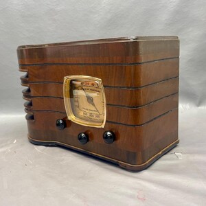 May include: A vintage wooden radio with a gold-colored dial and black knobs. The radio has a wood grain finish and is in good condition.