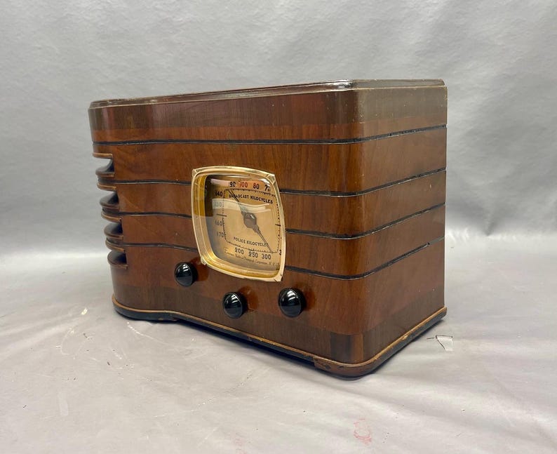 May include: A vintage wooden radio with a gold-colored dial and black knobs. The radio has a wood grain finish and is in good condition.