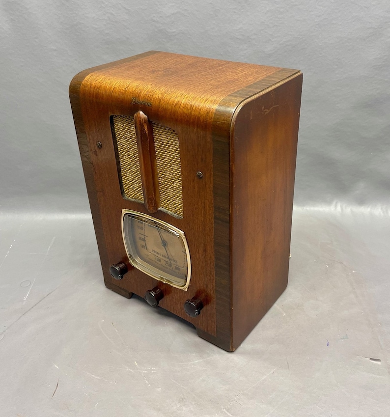 May include: A vintage wooden radio with a gold-colored dial and three knobs. The radio has a speaker grille with a wood trim and a label that reads "Emerson".