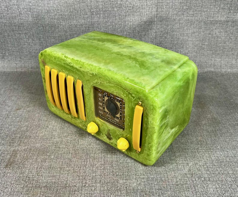 May include: A retro-style radio in a bright green colour with yellow detailing. The radio has a classic design with a dial, knobs, and speaker grill. The radio's face has a detailed display with numbers and a tuning dial. A decorative piece for home decor.