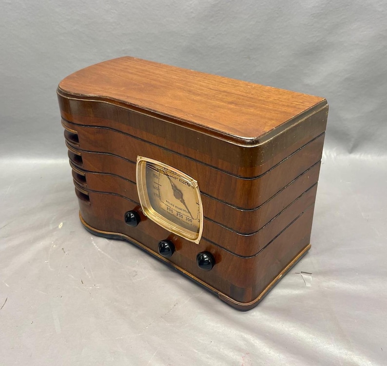 May include: A vintage wooden radio with a gold-colored dial and black knobs. The radio has a wood grain finish and is in good condition.