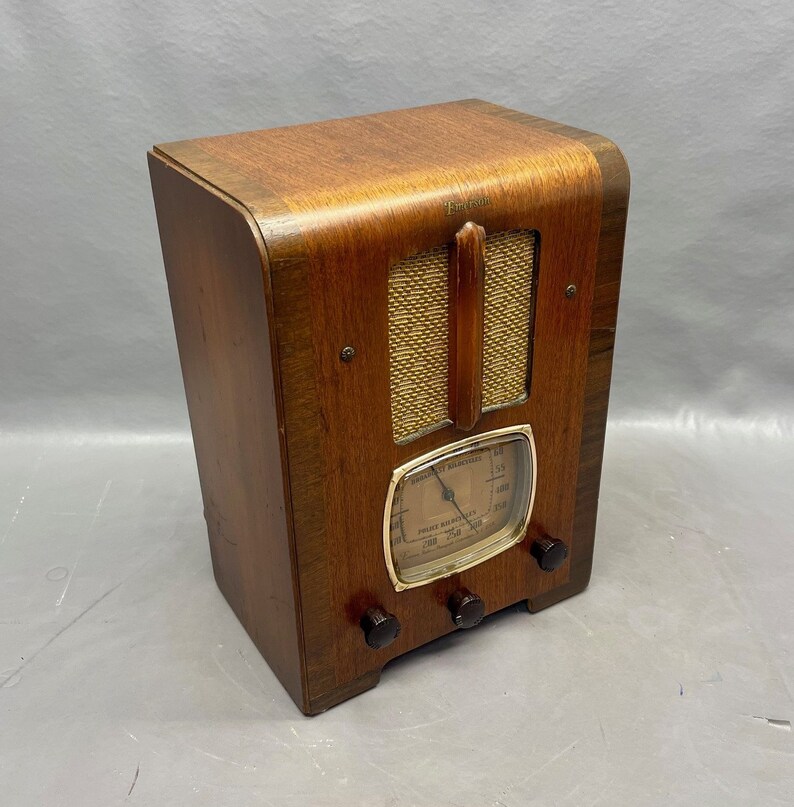 May include: A vintage wooden Emerson radio with a gold-colored dial and a speaker grille. The radio has a brown wooden cabinet and a gold-colored knob.