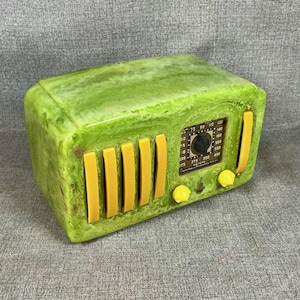 May include: A retro-style radio in green and yellow. The radio has a marbled green exterior with yellow accents, including vertical bars and knobs. The radio's face displays a dial and various markings.