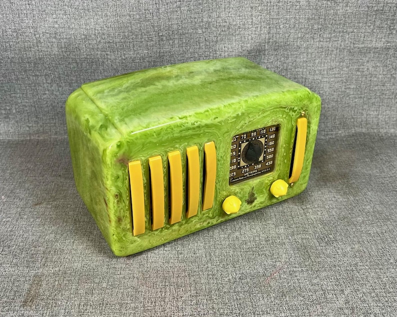 May include: A retro-style radio in green and yellow. The radio has a marbled green exterior with yellow accents, including vertical bars and knobs. The radio's face displays a dial and various markings.