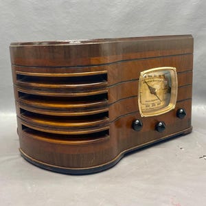 May include: A vintage wooden radio with a gold-colored dial and black knobs. The radio has a wood grain finish and a rectangular shape.