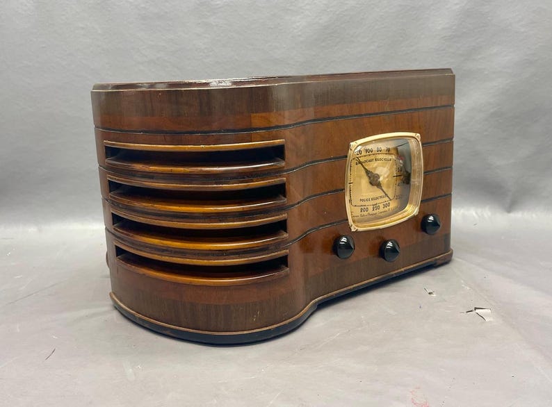 May include: A vintage wooden radio with a gold-colored dial and black knobs. The radio has a wood grain finish and a rectangular shape.