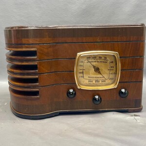 May include: A vintage wooden radio with a gold-colored dial and black knobs. The dial reads "Police Radiocycles" and has numbers from 120 to 300.