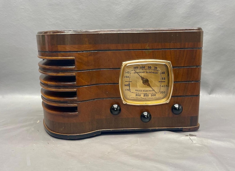 May include: A vintage wooden radio with a gold-colored dial and black knobs. The dial reads "Police Radiocycles" and has numbers from 120 to 300.