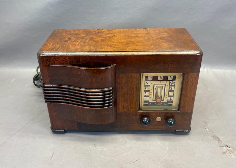 Może przedstawiać: Antyczne drewniane radio z brązową drewnianą obudową i srebrną płytą czołową. Radio ma pokrętło z liczbami od 55 do 160 i tekstem "Frequency Range".