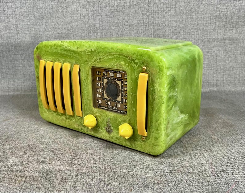May include: A vintage green radio with yellow detailing. The radio has a rectangular form with a dial and speaker grilles. The face of the radio features a dial and a small display with numbers. The radio is a retro style.