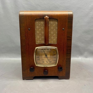 May include: A vintage wooden Emerson radio with a gold-colored dial and a speaker grille. The dial has markings for "Broadcast Band" and "Police Kilocycles".