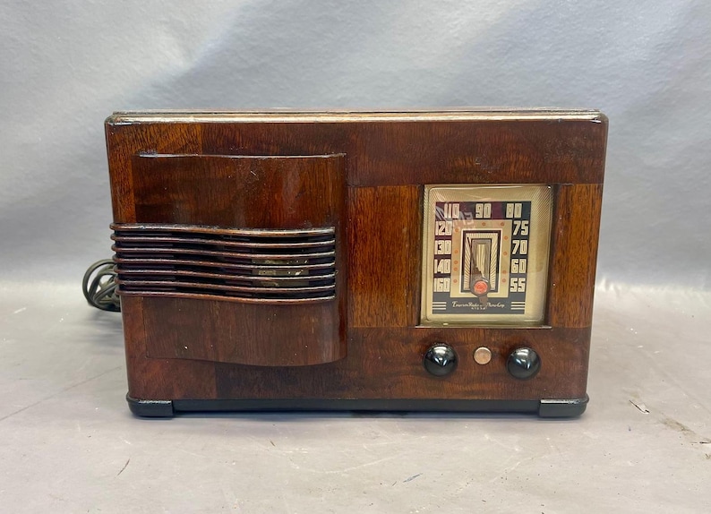 Może przedstawiać: Antyczne drewniane radio z ciemnobrązowym wykończeniem i srebrnym pokrętłem. Pokrętło ma czarną wskaz&oacute;wkę i białe cyfry. Radio ma dwa pokrętła z przodu.
