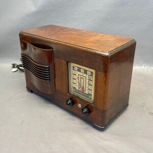 Może przedstawiać: Antyczne drewniane radio z brązową drewnianą obudową i srebrną płytą czołową. Radio ma tarczę z liczbami od 55 do 110. Radio ma dwa pokrętła z przodu.