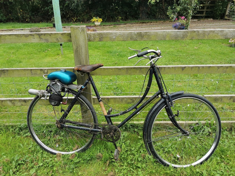 May include: A black bicycle with a teal gas tank and a brown leather seat. The bicycle has a motor attached to the rear wheel.