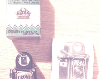 May include: A vintage Coronet Midget camera with a black and silver body. The camera is 13x18 mm and takes perfect miniature pictures. The box is green and white with a crown logo and the text "Coronet Midget Camera".