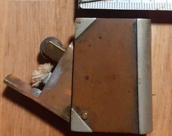 Peut inclure: Un briquet vintage en cuivre et argent avec une mèche et une roue pour créer une étincelle. Le briquet est fermé et a une forme rectangulaire.