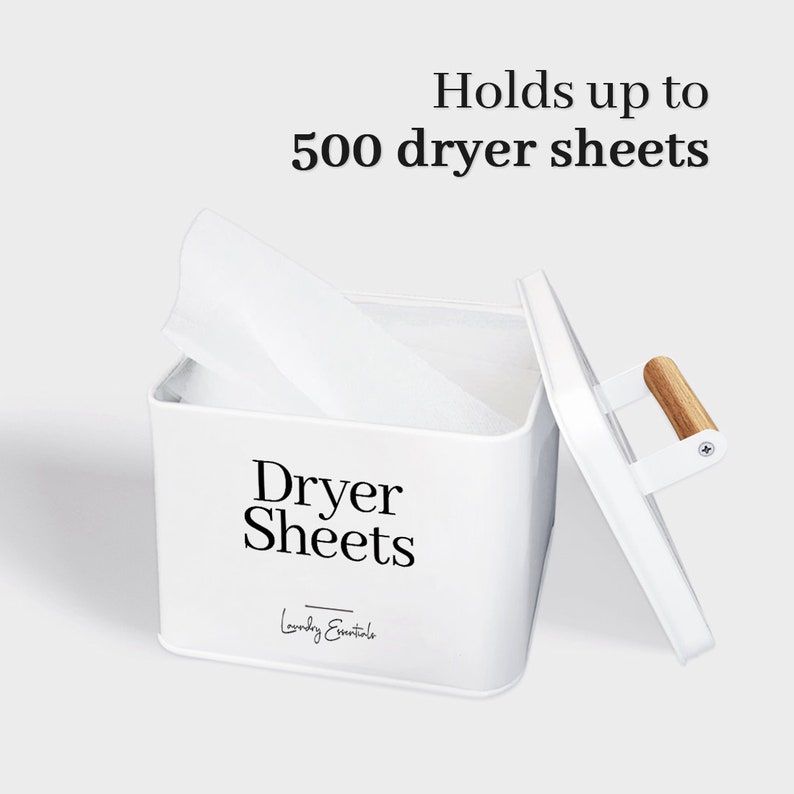 May include: White metal storage container with a wooden handle, labeled "Dryer Sheets" and "Laundry Essentials". The container is open and has a dryer sheet inside. The text "Holds up to 500 dryer sheets" is above the container.
