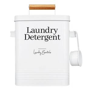 May include: White metal laundry detergent container with a wooden handle and a scoop. The container has the text "Laundry Detergent" and "Laundry Essentials" printed on it.