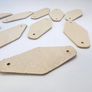 May include: A collection of ten off-white leather keychains with a diamond shape and a hole in the top.