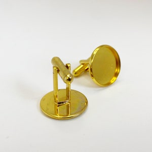 May include: A pair of gold-toned cufflinks with round, smooth, blank surfaces. The cufflinks are made of metal and have a polished finish.