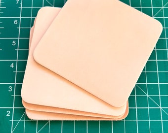 May include: A stack of four light pink leather squares on a green cutting mat.