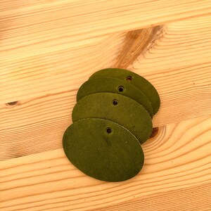 Könnte beinhalten: Vier ovale Lederanhänger in dunkelgrüner Farbe. Jeder Anhänger hat ein Loch in der Mitte.