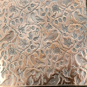 May include: A copper-coloured metal tile with an embossed design of birds and leaves. The tile has a repeating pattern of birds perched on branches with leaves and berries.