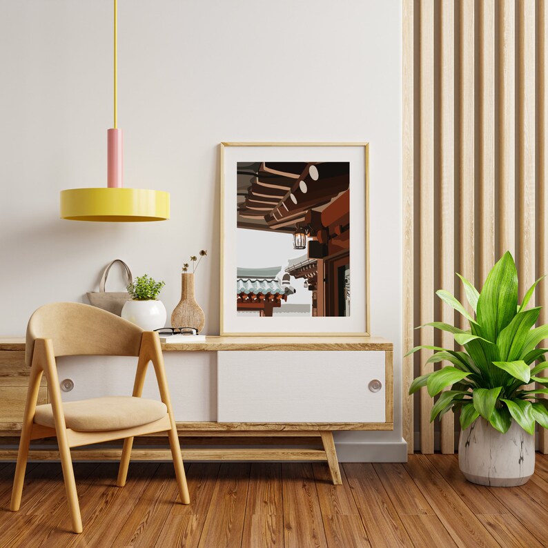 May include: A framed print of a traditional Asian building with a wooden roof and a lantern hanging from the eaves. The building is painted in shades of brown and red, and the roof is covered in blue tiles. The print is hanging on a white wall above a wooden cabinet.