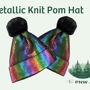 Puede incluir: Dos gorros de punto metálico arcoíris con pompones de piel sintética negra. Los gorros están doblados por la mitad y la imagen tiene un fondo verde claro.