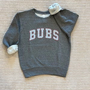 May include: Gray sweatshirt with the word "CUBS" in white letters with red stitching around the letters.