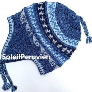 Könnte beinhalten: Blaue Strickmütze mit geometrischem Muster und einem geflochtenen Bommel. Die Mütze hat Ohrenklappen und einen umgeschlagenen Rand.