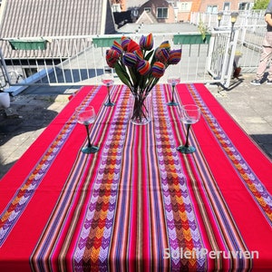 May include: A red and white striped tablecloth with a colorful geometric pattern. The tablecloth is laid out on a table with four wine glasses and a bouquet of colorful tulips in a glass vase.