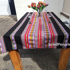 Puede incluir: Mantel de mesa negro y a rayas de colores con un patrón geométrico. El mantel está puesto sobre una mesa de madera con un jarrón de flores de colores en el centro.