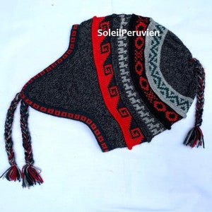 Può includere: Un cappello di lana grigio, rosso e verde con un lungo pon pon intrecciato. Il cappello ha un motivo geometrico e il testo "SoleilPeruvien" è stampato sul lato.