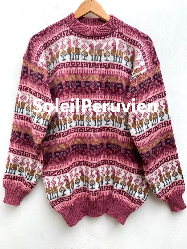 May include: A pink alpaca sweater with a traditional Peruvian design. The sweater features a geometric pattern with llamas and other animals.