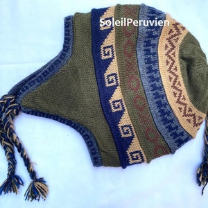 Puede incluir: Un gorro de punto verde, azul y marrón con una larga borla trenzada. El gorro tiene un patrón geométrico y el texto "SoleilPeruvien" es visible en el gorro.