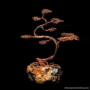 May include: A copper wire sculpture of a bonsai tree with a twisted trunk and branches. The tree is sitting on a rock base.