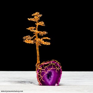 May include: A gold wire tree sculpture with a purple agate base. The tree is made of thin wire and has a delicate, intricate design. The agate base is a natural stone with a unique pattern and color.