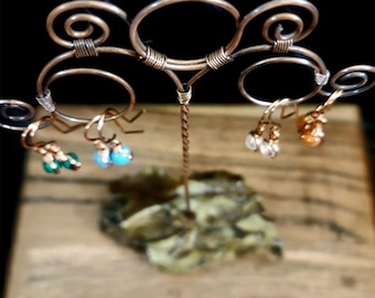 May include: A copper wire earring display stand with three tiers. The stand is holding three pairs of earrings with turquoise, green, and orange stones.